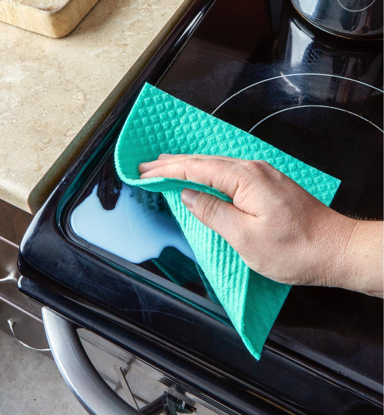 Wiping up a liquid spill on a stovetop using a reusable household paper towel