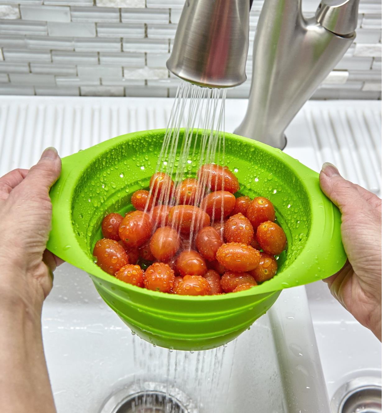 Petite passoire compressible tenue sous un robinet pour rincer des tomates raisins