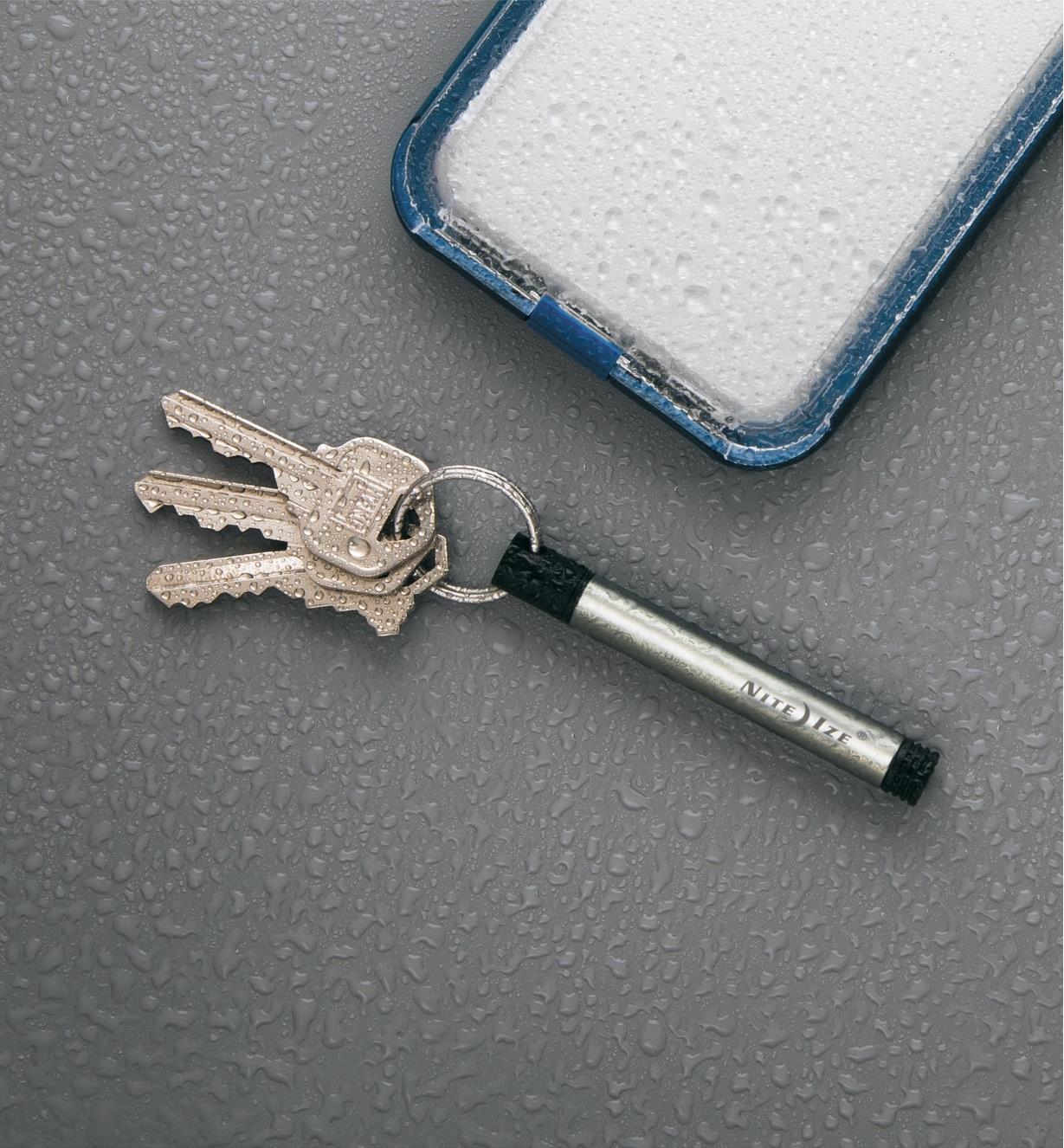 Inka Adventure Pen attached to set of keys and lying next to a cell phone, sprinkled with water