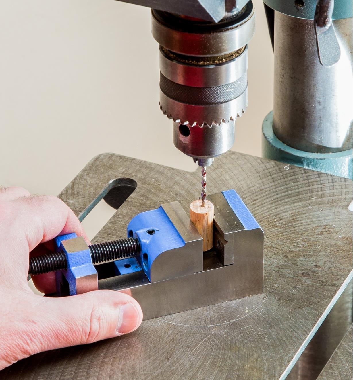 A drill press is used to drill a hole in a small piece of wood that is held in the toolmaker’s vise.