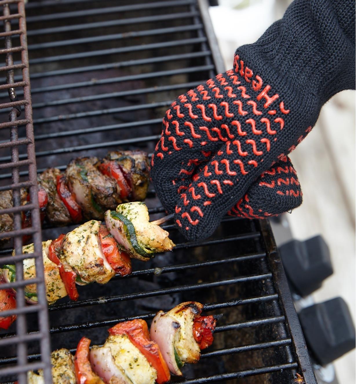 Wearing barbecue gloves to turn skewers on barbecue.