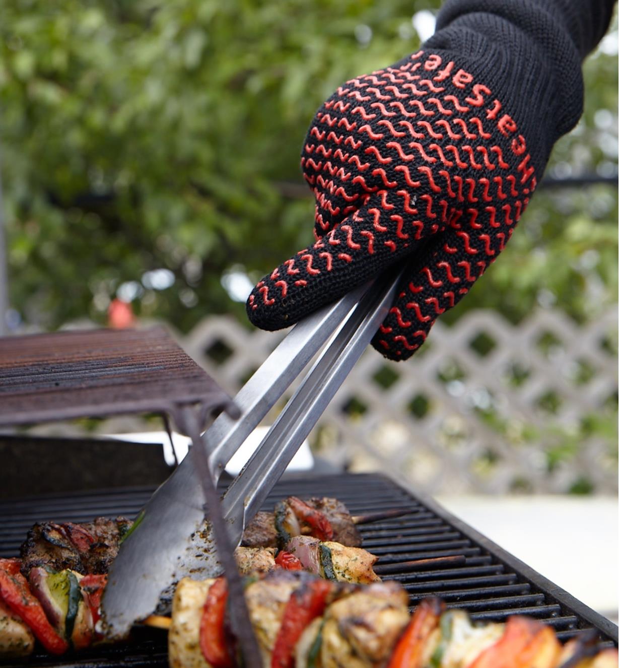 Wearing barbecue gloves while using tongs to turn food on barbecue.