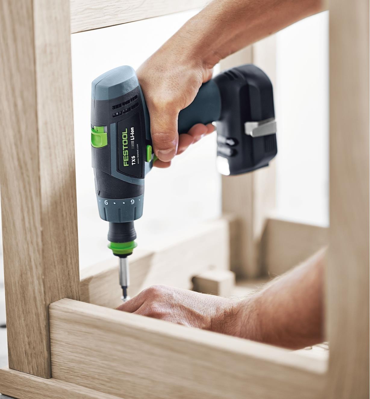 Driving a screw into the underside of a chair with a TXS Cordless Drill