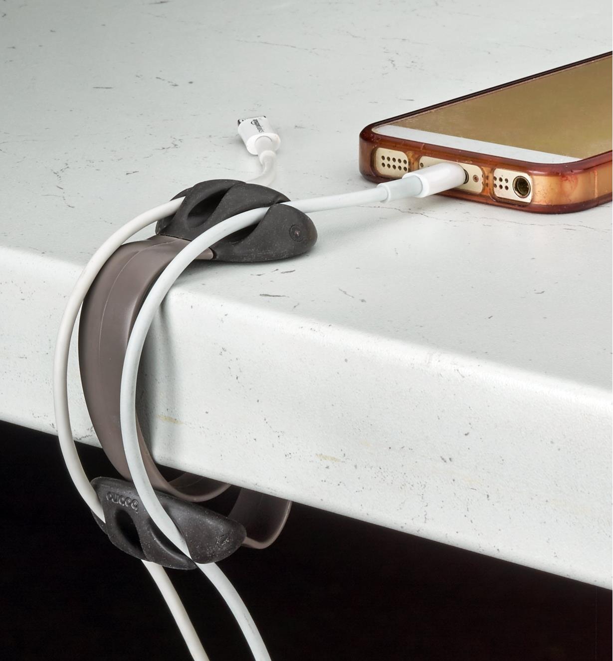 Charcoal clip attached to a table, holding two charger cables