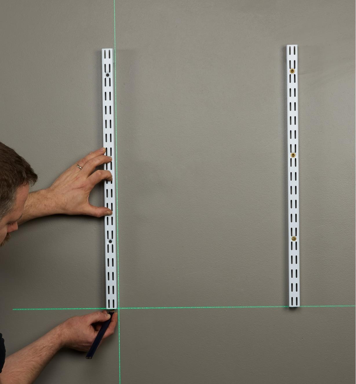 A green crosshair laser level beam is projected onto a wall, allowing an installer to ensure shelf tracking is level and plumb