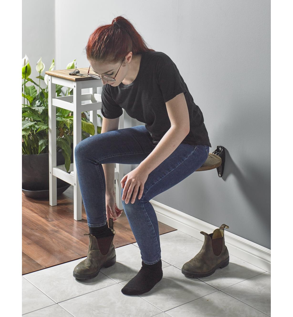 A woman sits on a hall seat while putting on boots