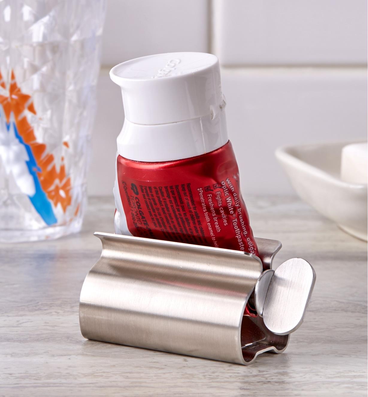 The tube squeezer holding a rolled-up tube sits on a bathroom counter