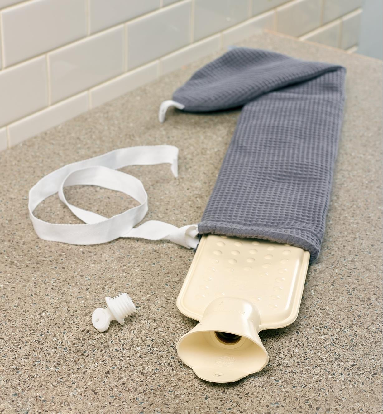 An empty long hot-water bottle sits on a counter, the cover partially removed, ready to fill