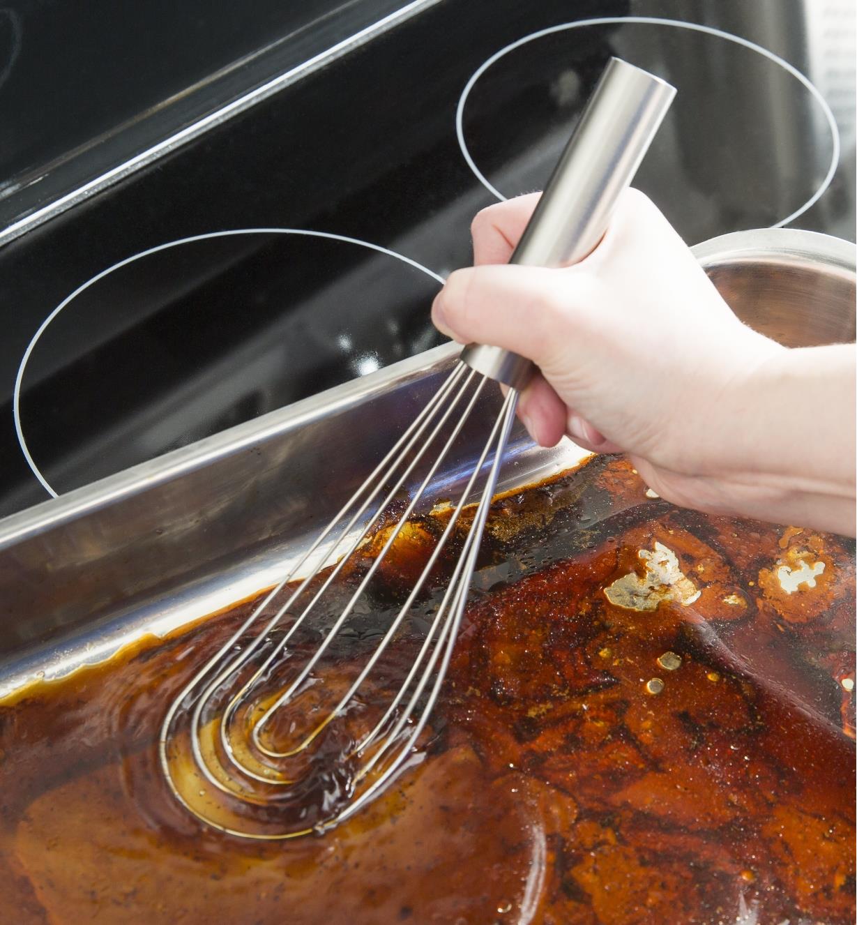 Using a 10" flat whisk to mix meat juices in a pan