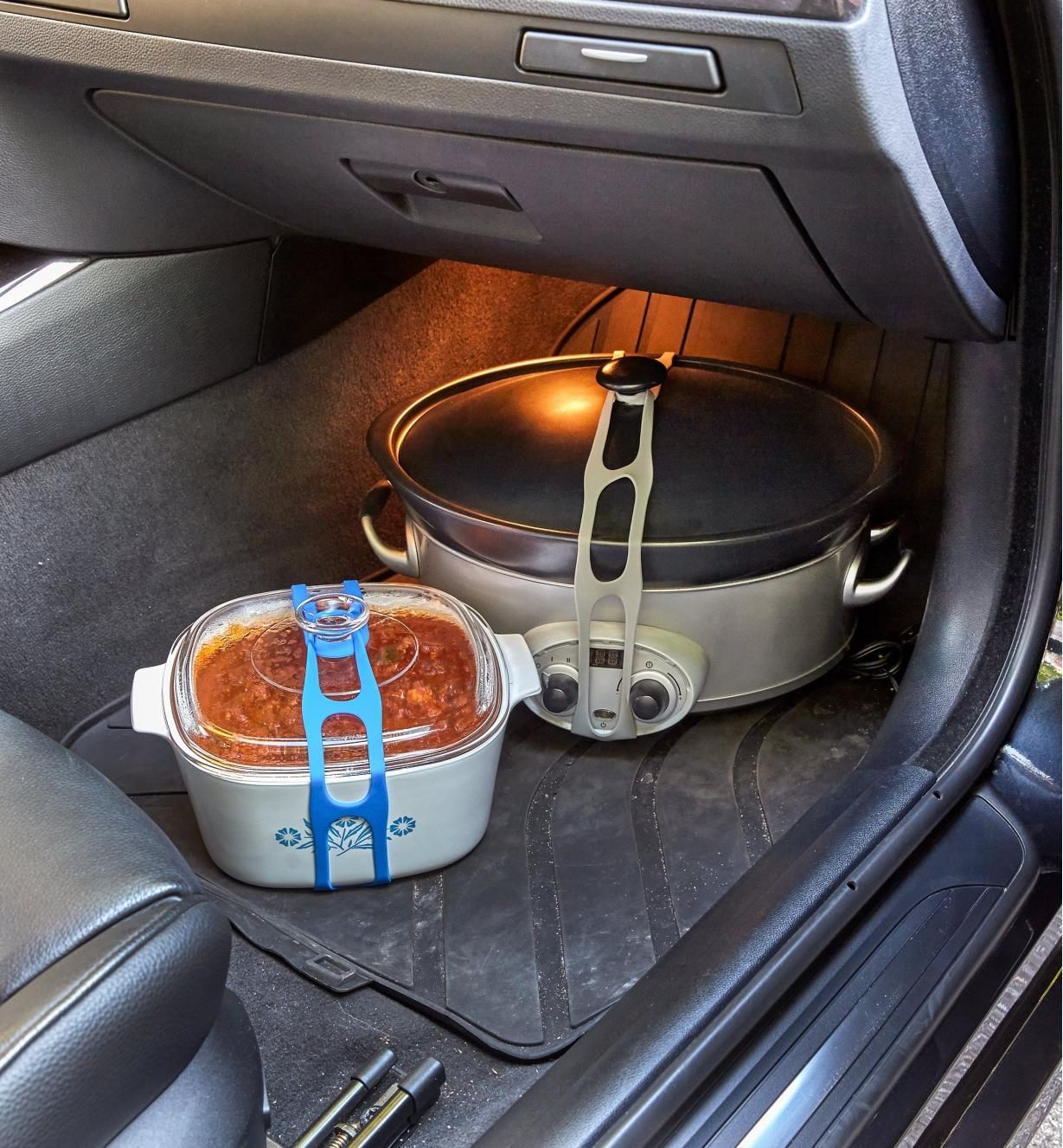 Casserole dish and slow-cooker pot held closed with lid latches in a car’s passenger-side footwell