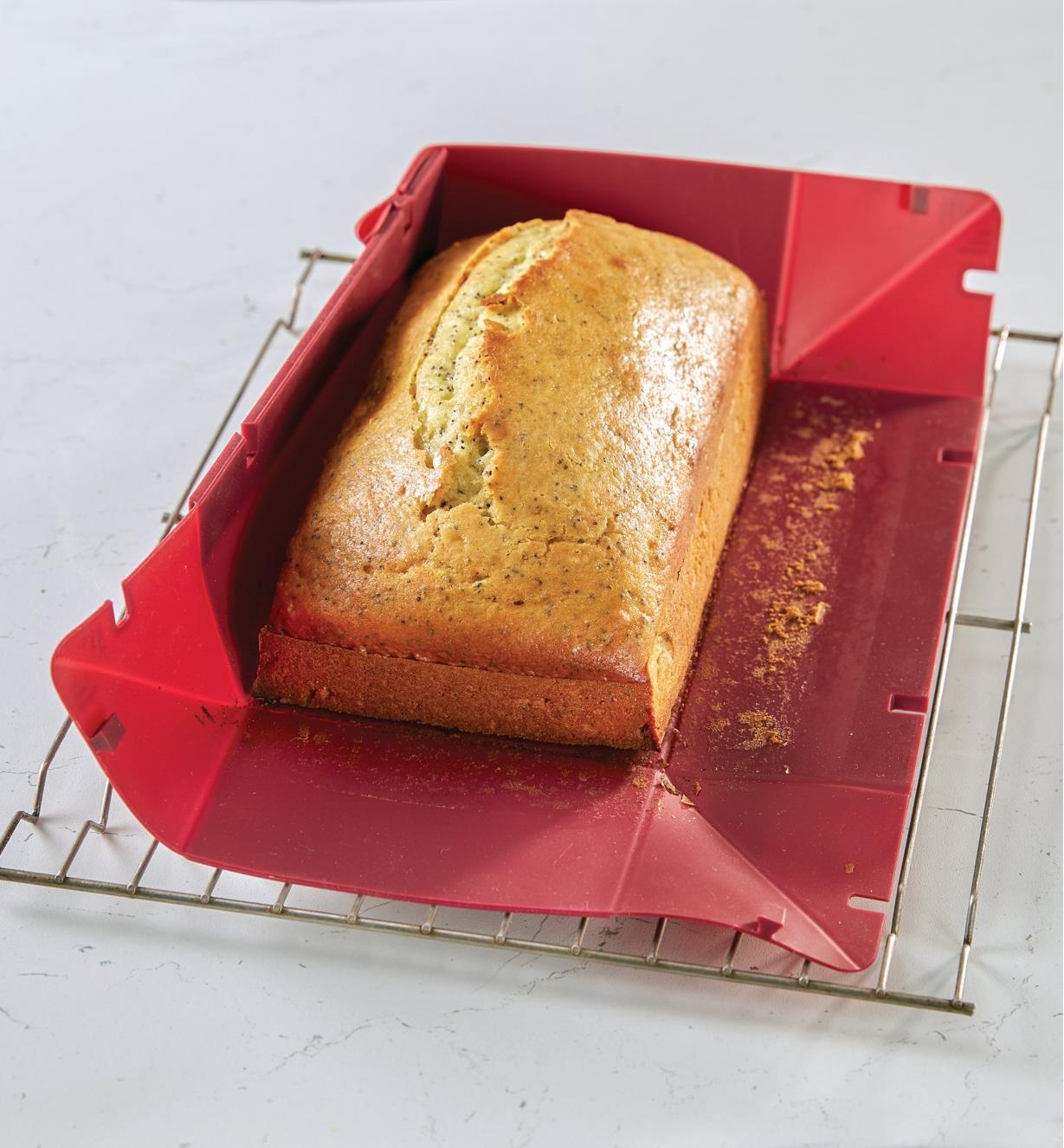 The sides of the collapsible silicone loaf pan are detached to remove a freshly baked loaf
