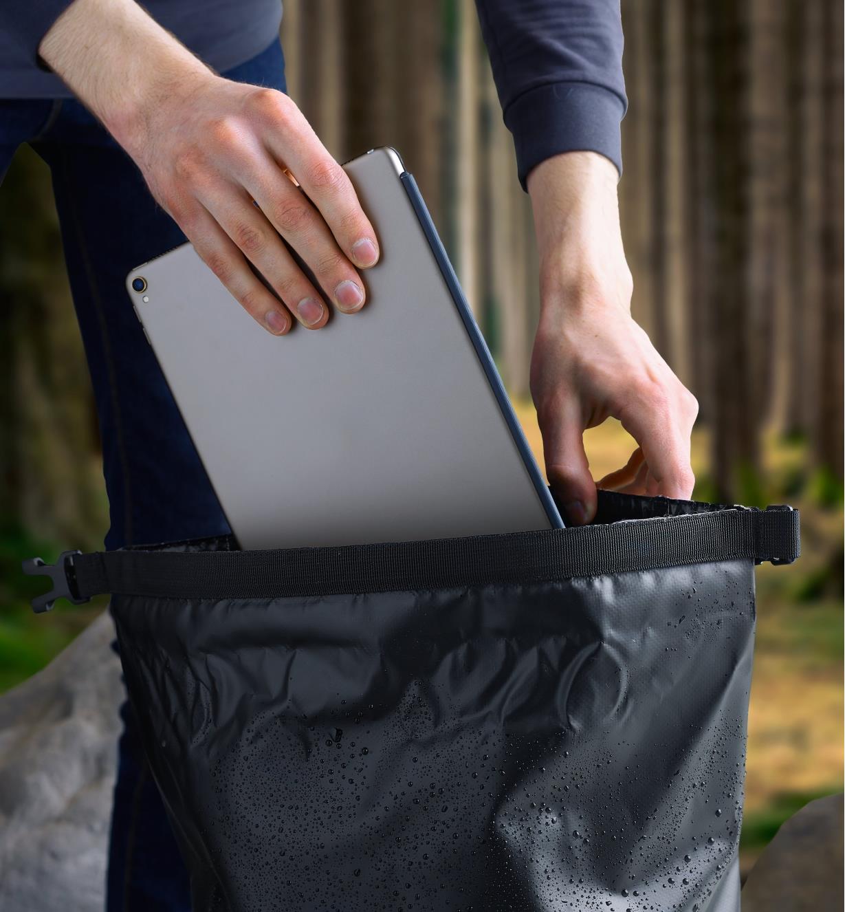 A tablet is placed inside the waterproof dry bag backpack through the roll-top opening