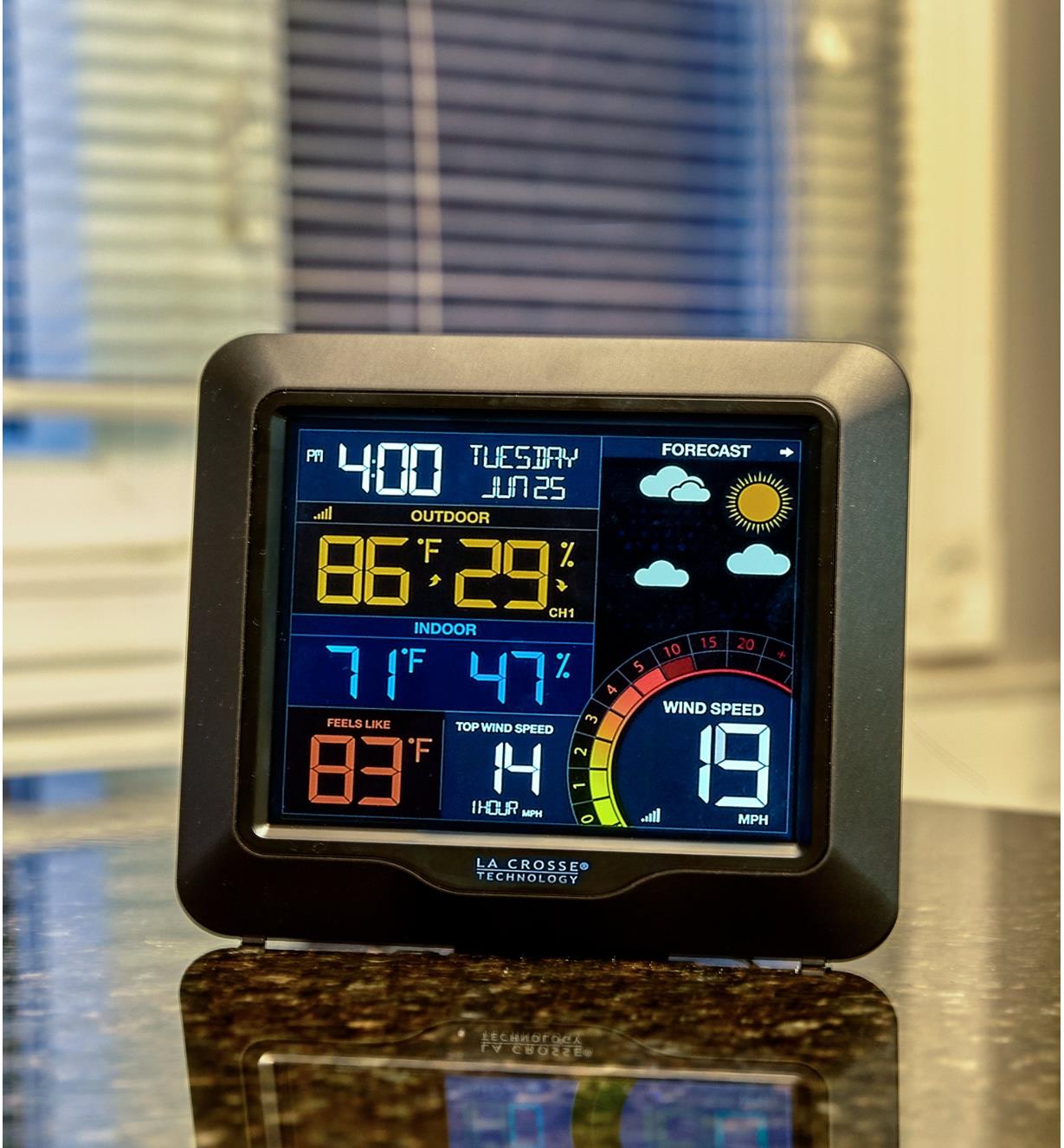 LCD screen of the wireless weather station displays date, time, forecast icons, temperature and humidity in Fahrenheit and wind speed in miles per hour