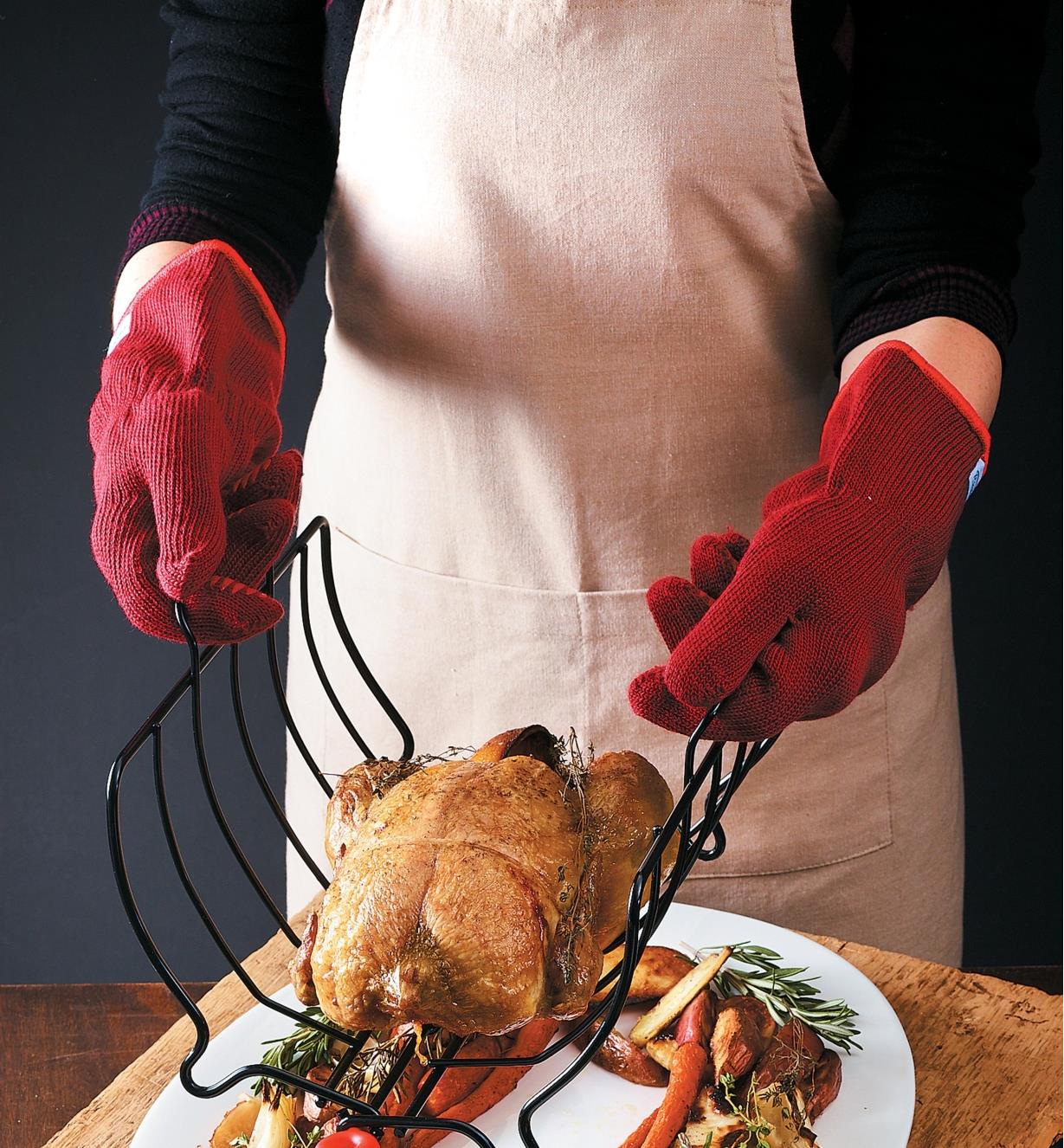 Oven gloves protect hands when transferring a roasted chicken from a pan to a serving plate