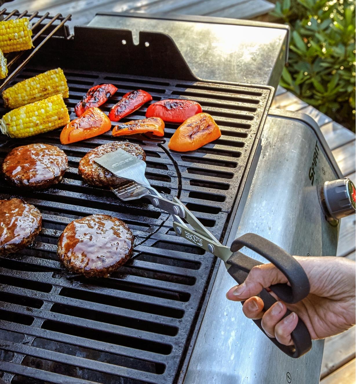BBQ Croc tongs picking up a hamburger in the center of a grill