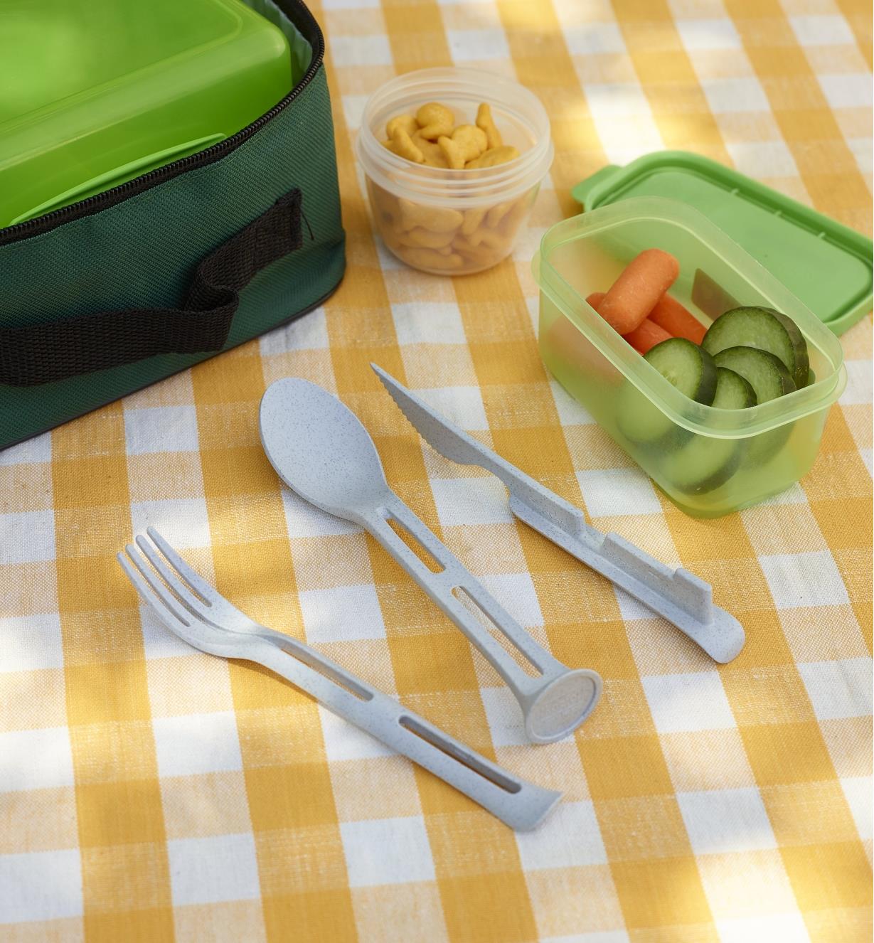 Gray Klikk small cutlery set taken apart to show the knife, fork and spoon next to containers of food