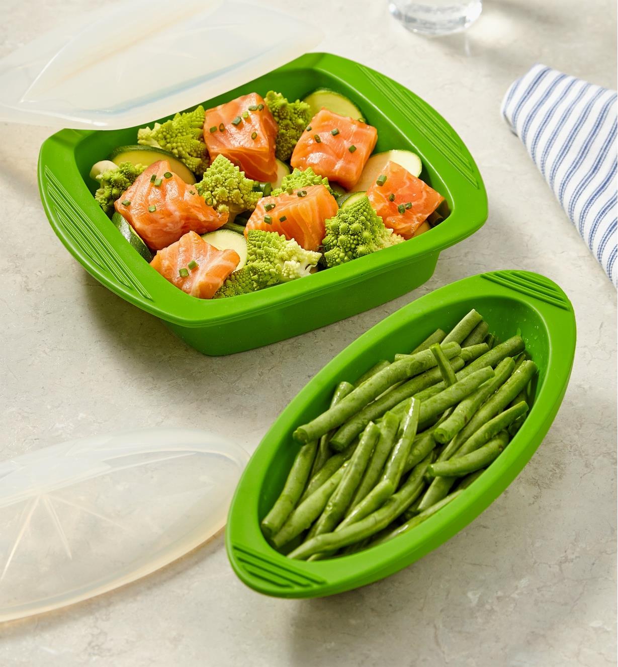 Deux papillotes en silicone utilisées pour cuire des haricots verts ainsi qu'un plat de saumon et de légumes