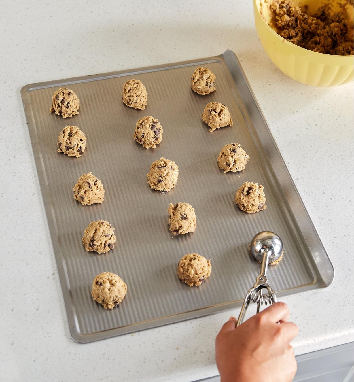 Personne formant des boules de pâte à biscuits sur une plaque à biscuits avec une cuillère