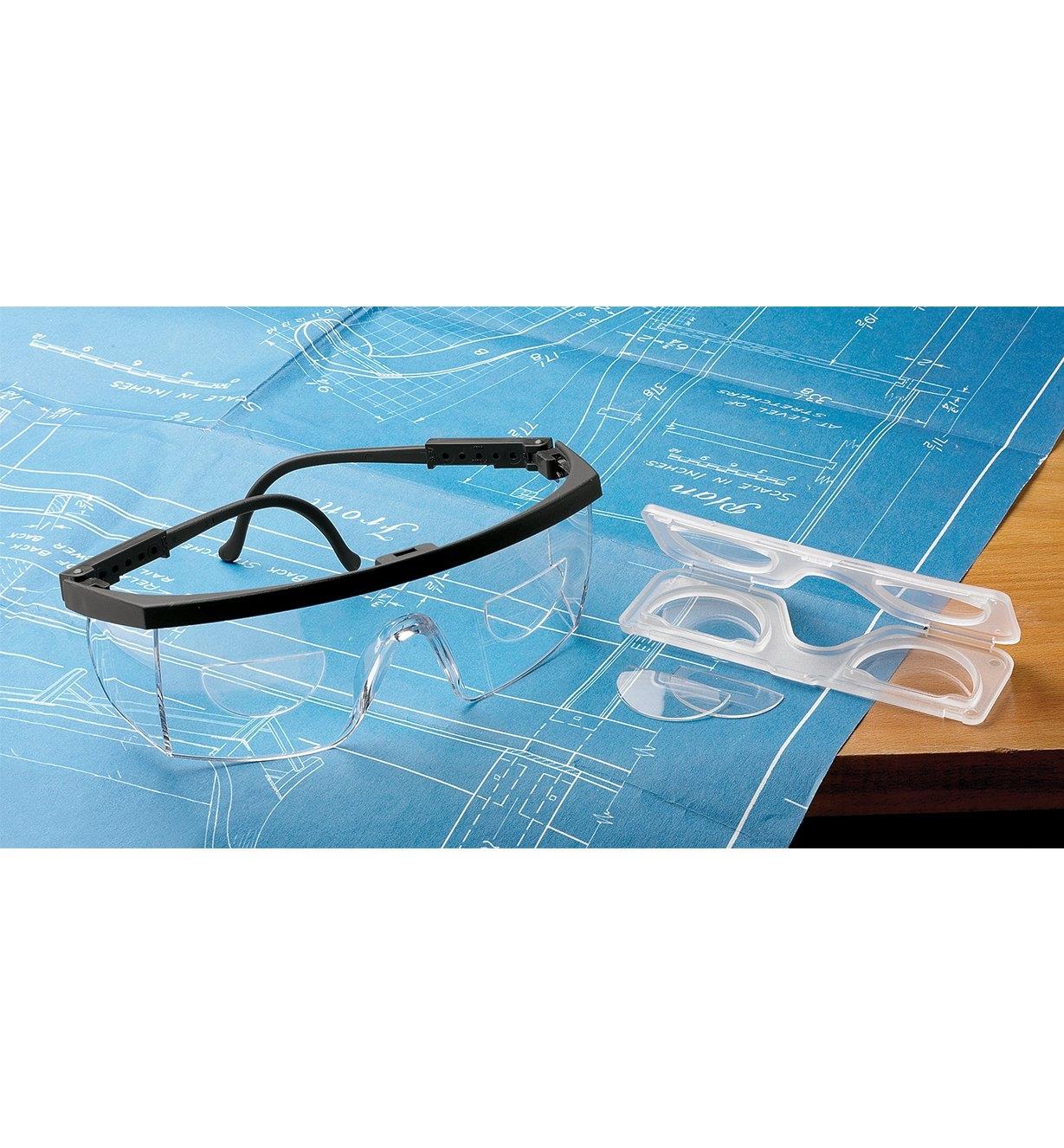Magnifying lenses and case beside a pair of safety glasses with magnifying lenses applied