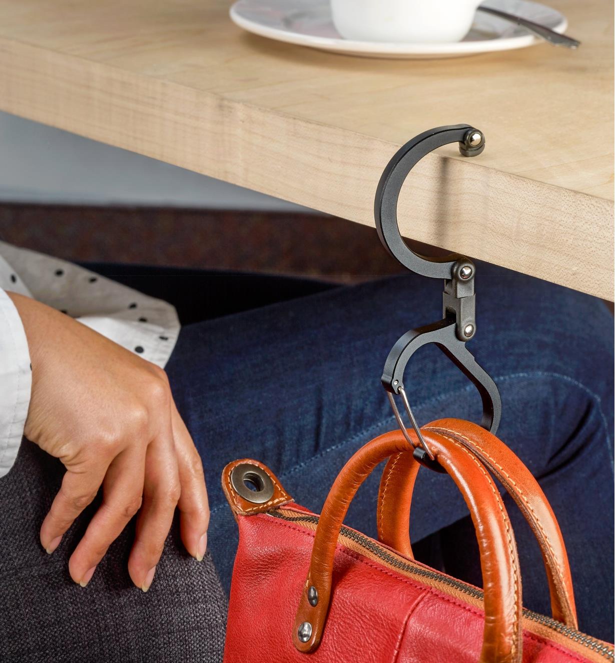 A Heroclip carabiner used to hang a purse on the edge of a table in a restaurant