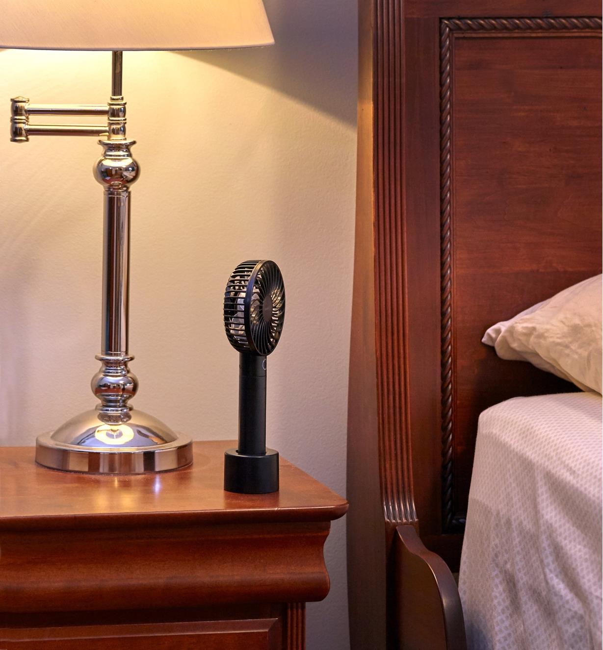 A rechargeable portable turbo fan standing on its non-slip base on a night table beside a bed