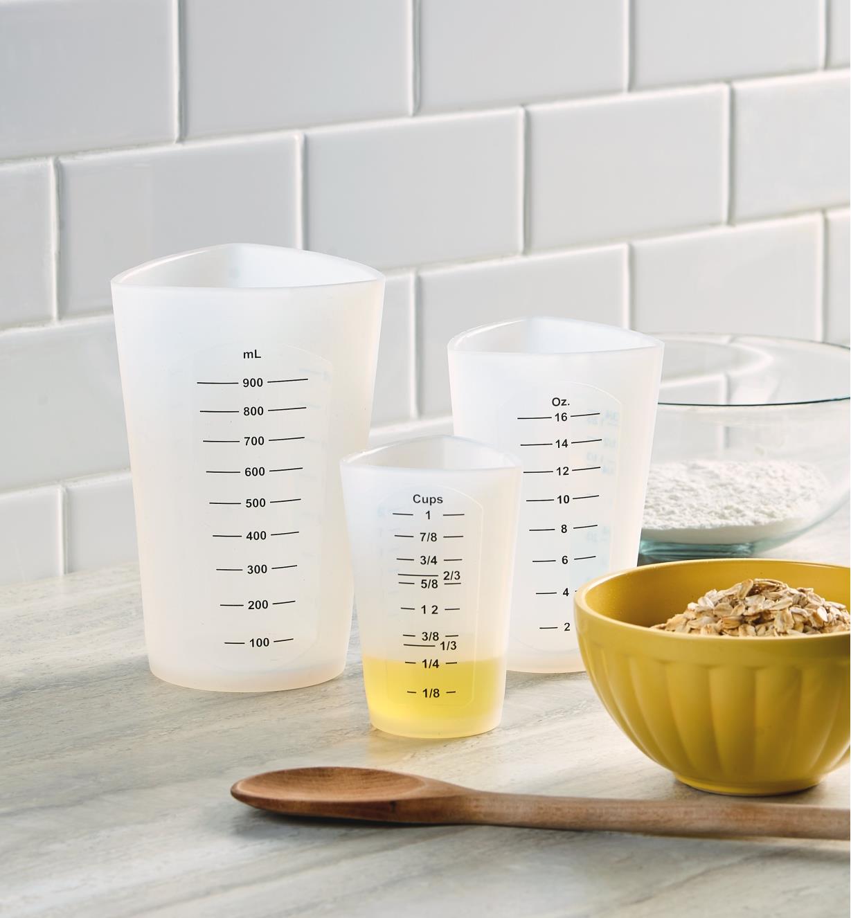 Three sizes of flexible silicone measuring cups on a countertop with the liquid level in the smallest size clearly visible through the side