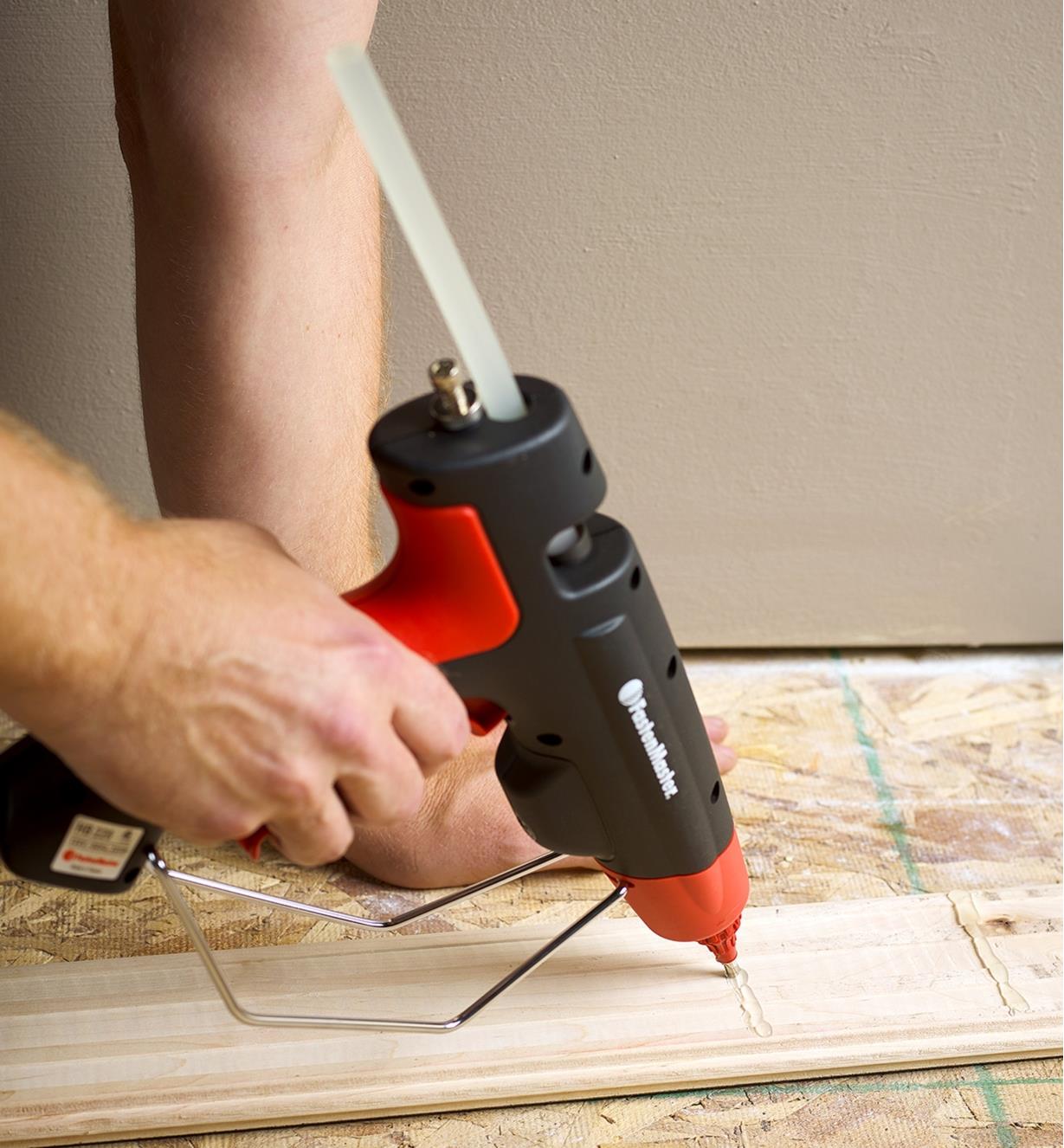 A FastenMaster pro hot-melt gun being used to apply glue to a piece of wooden flooring