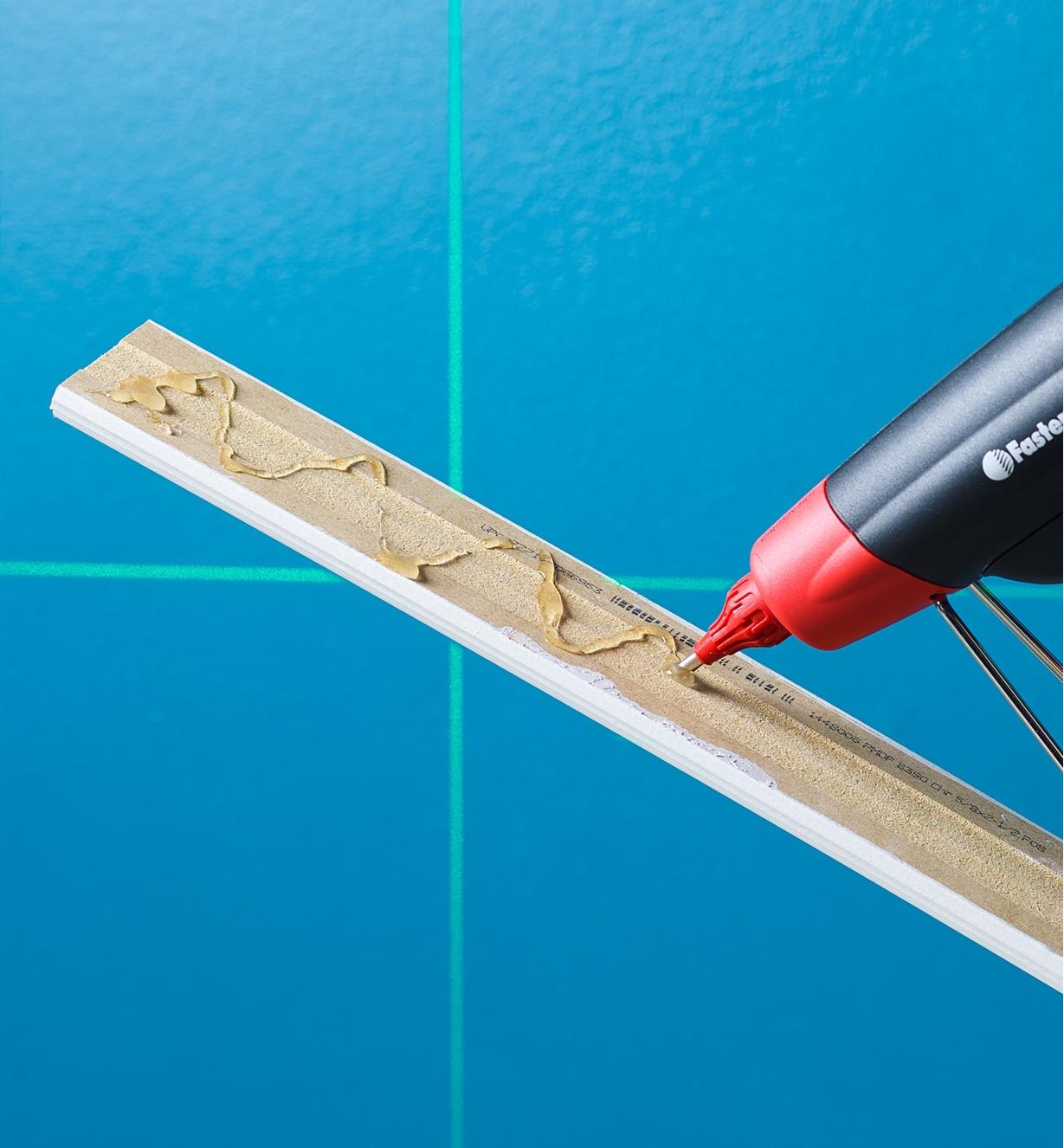 Installing a piece of trim molding, using a FastenMaster pro hot-melt gun to glue it in place