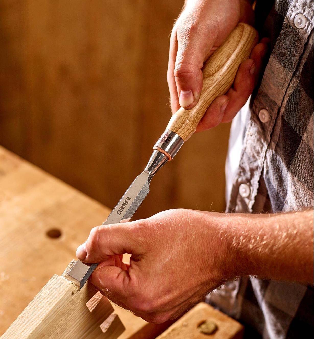 A woodworker uses a 3/4" Narex Richter chisel to trim the tails of a large dovetail joint