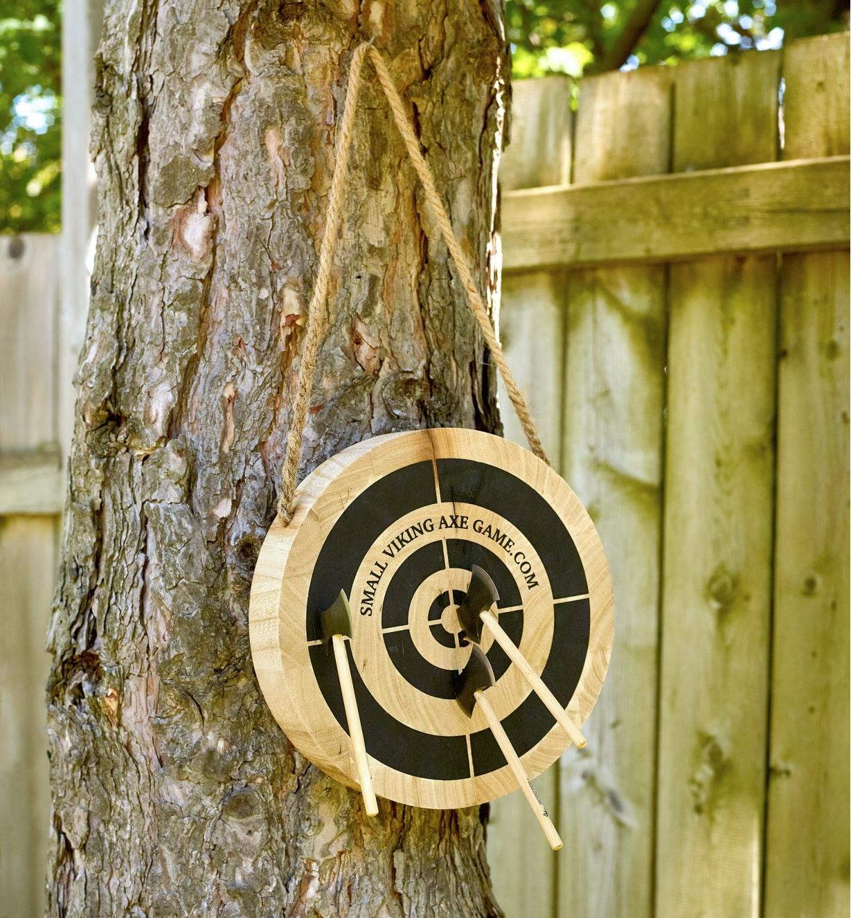 Three miniature axes embedded in a wooden target hung from a backyard tree