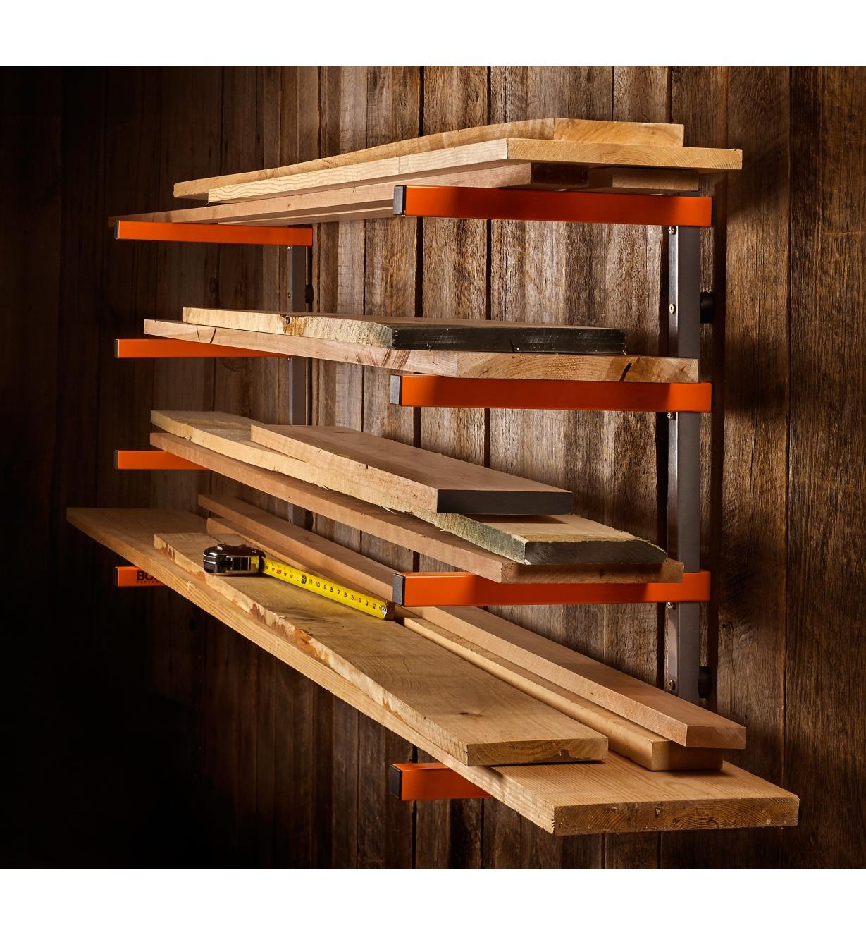 Various sizes of wooden boards stacked on a Bora four-shelf lumber rack mounted on a barnboard wall