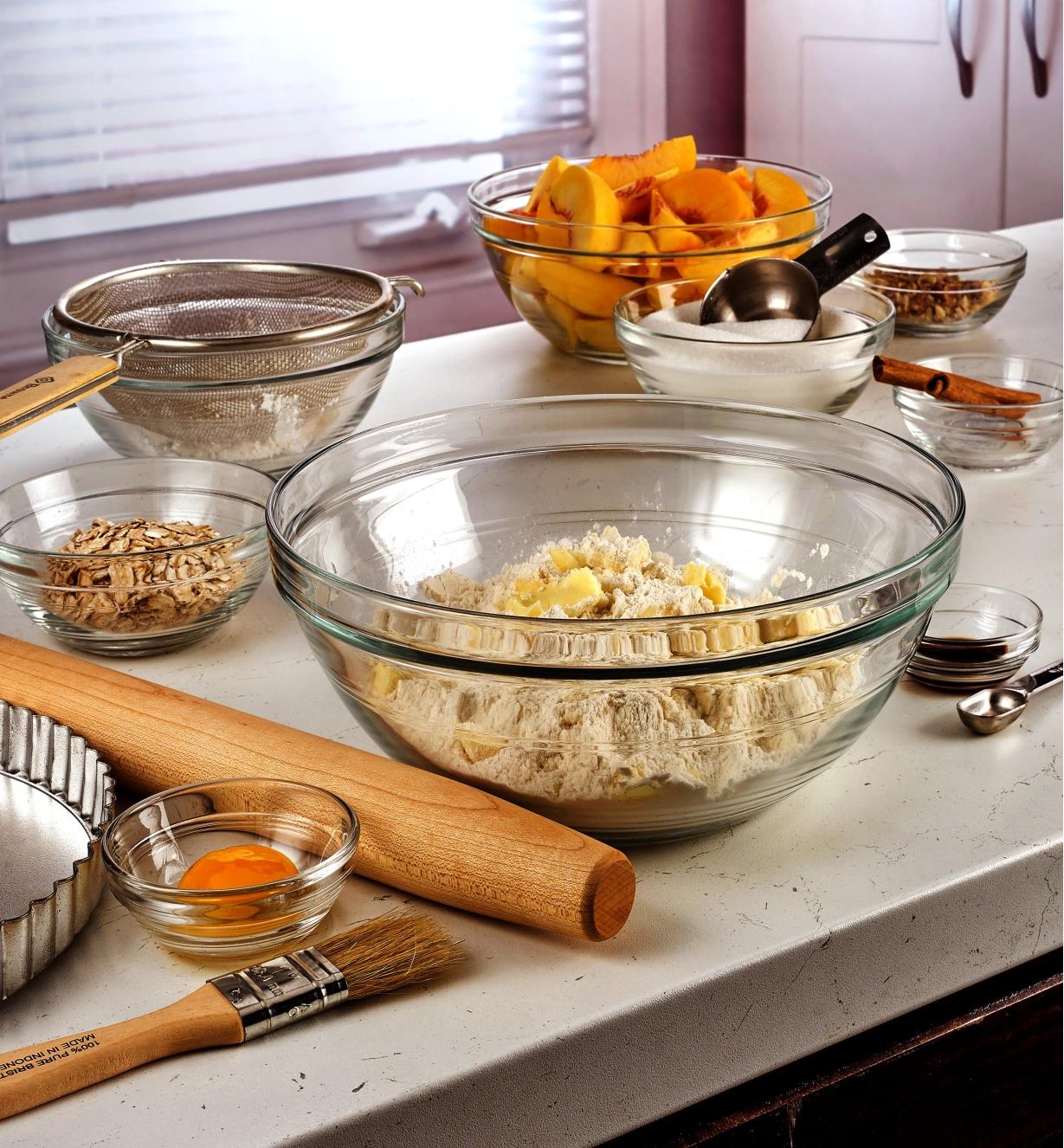 Various sizes of Duralex glass bowls being used to contain and mix ingredients to make a peach pie