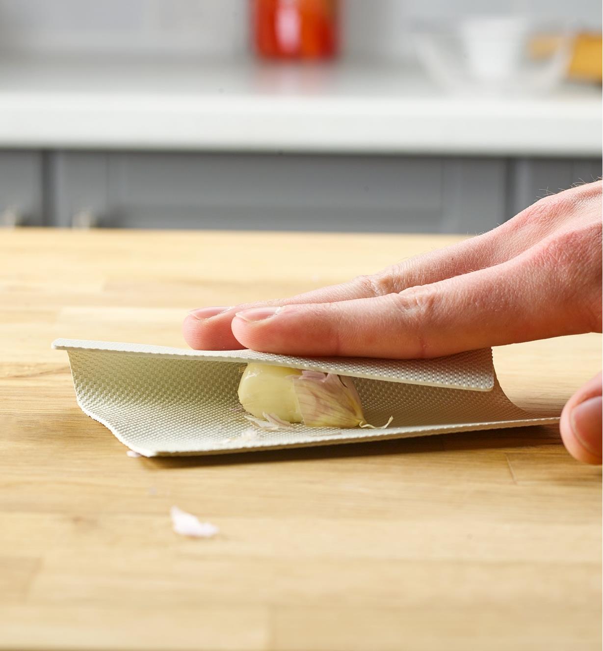 Peeling a garlic clove on a countertop using the garlic peeling mat