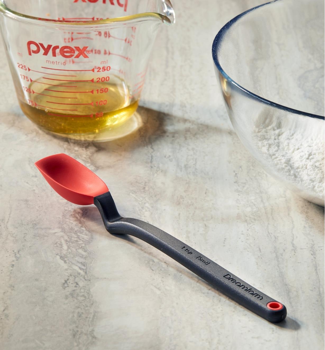 The mini spoon-spatula on a countertop near a glass measuring cup and mixing bowl