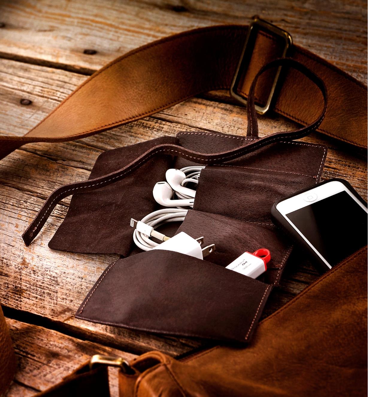 Étui en cuir contenant un câble de recharge, des écouteurs et une clé USB près d'un téléphone intelligent et d'un sac à main