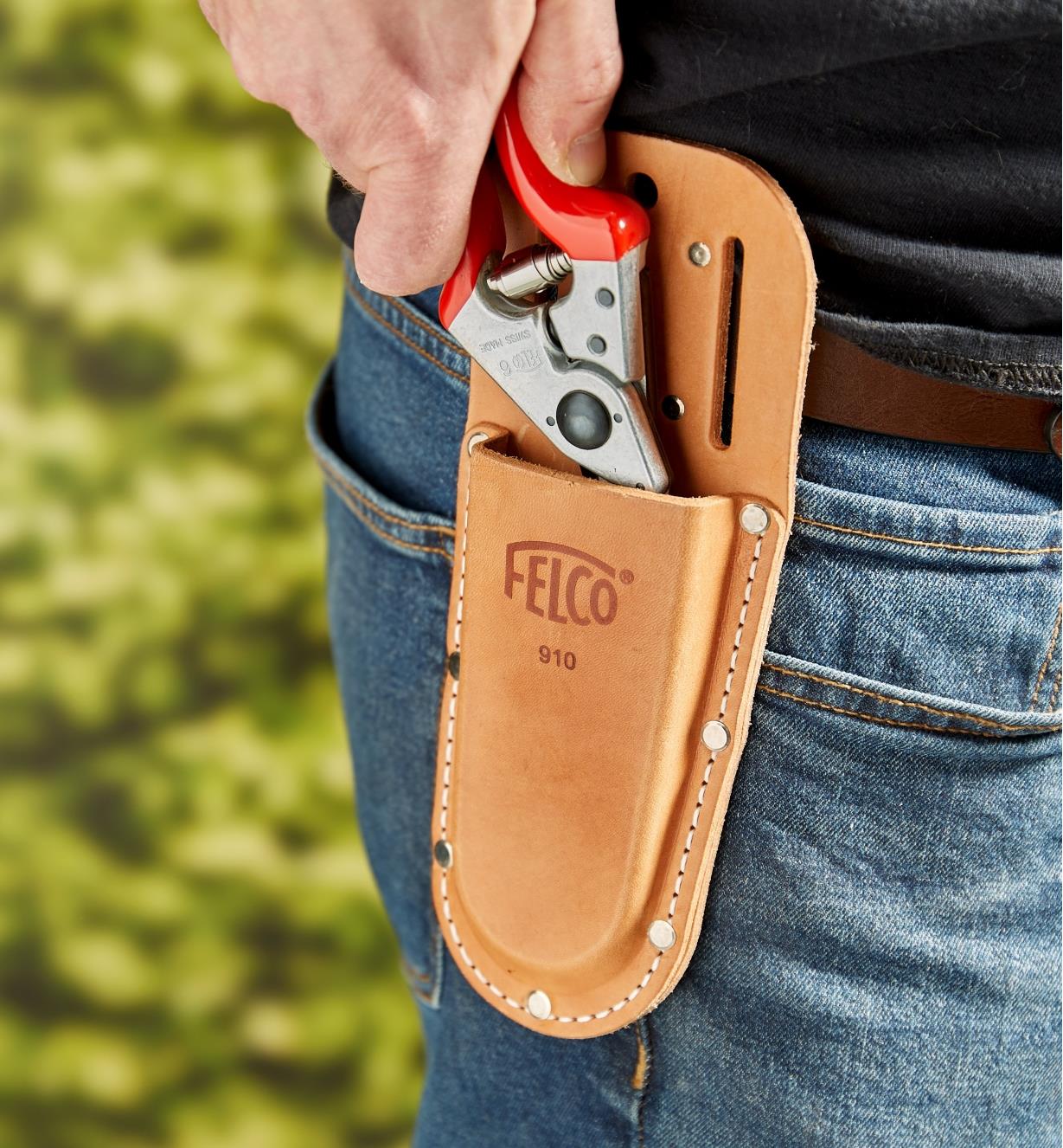A gardener slips a Felco hand pruner into a pruner holster worn on the hip