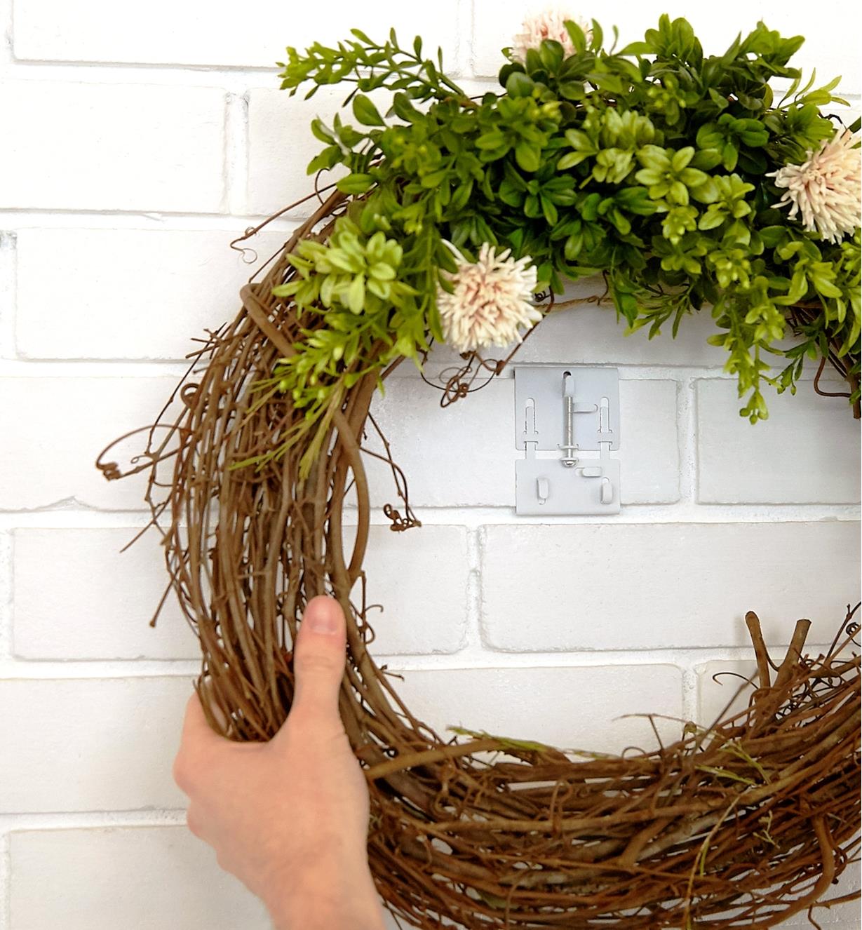 A wreath is hung on a brick wall with a brick clamp that is painted to match the wall