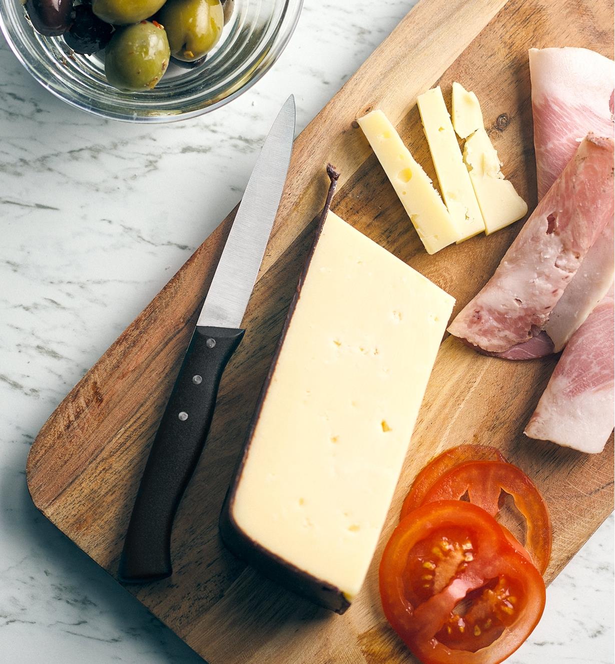 The serrated paring knife on a board with meat, cheese and tomato slices