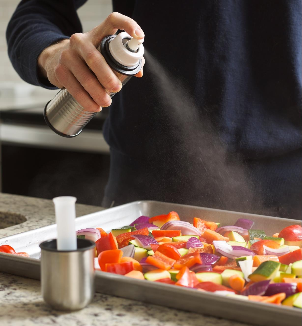 Spraying a baking tray of vegetables with the oil mister