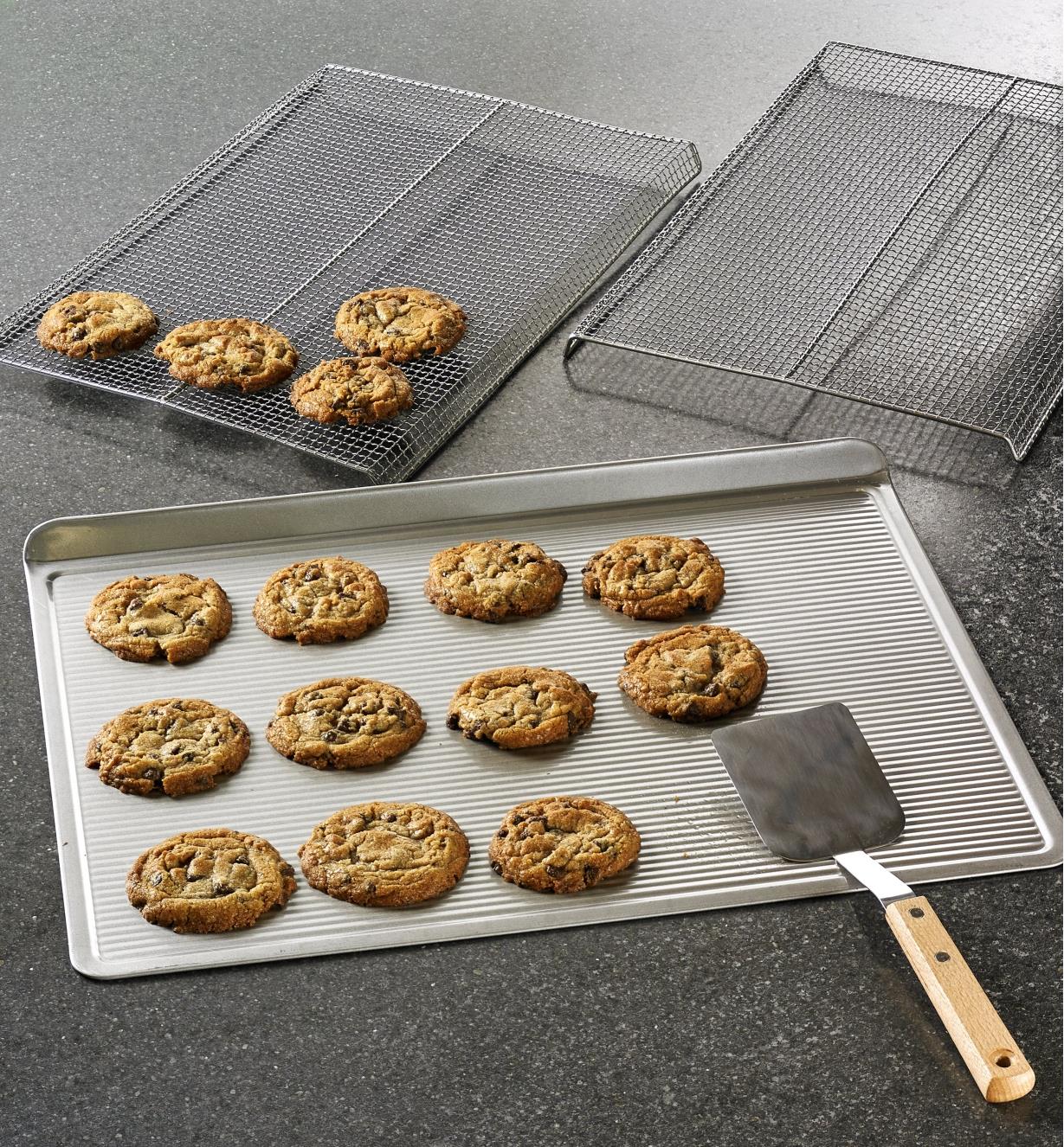 The cookie sheet, cookie racks and stainless-steel spatula being used to make a batch of cookies