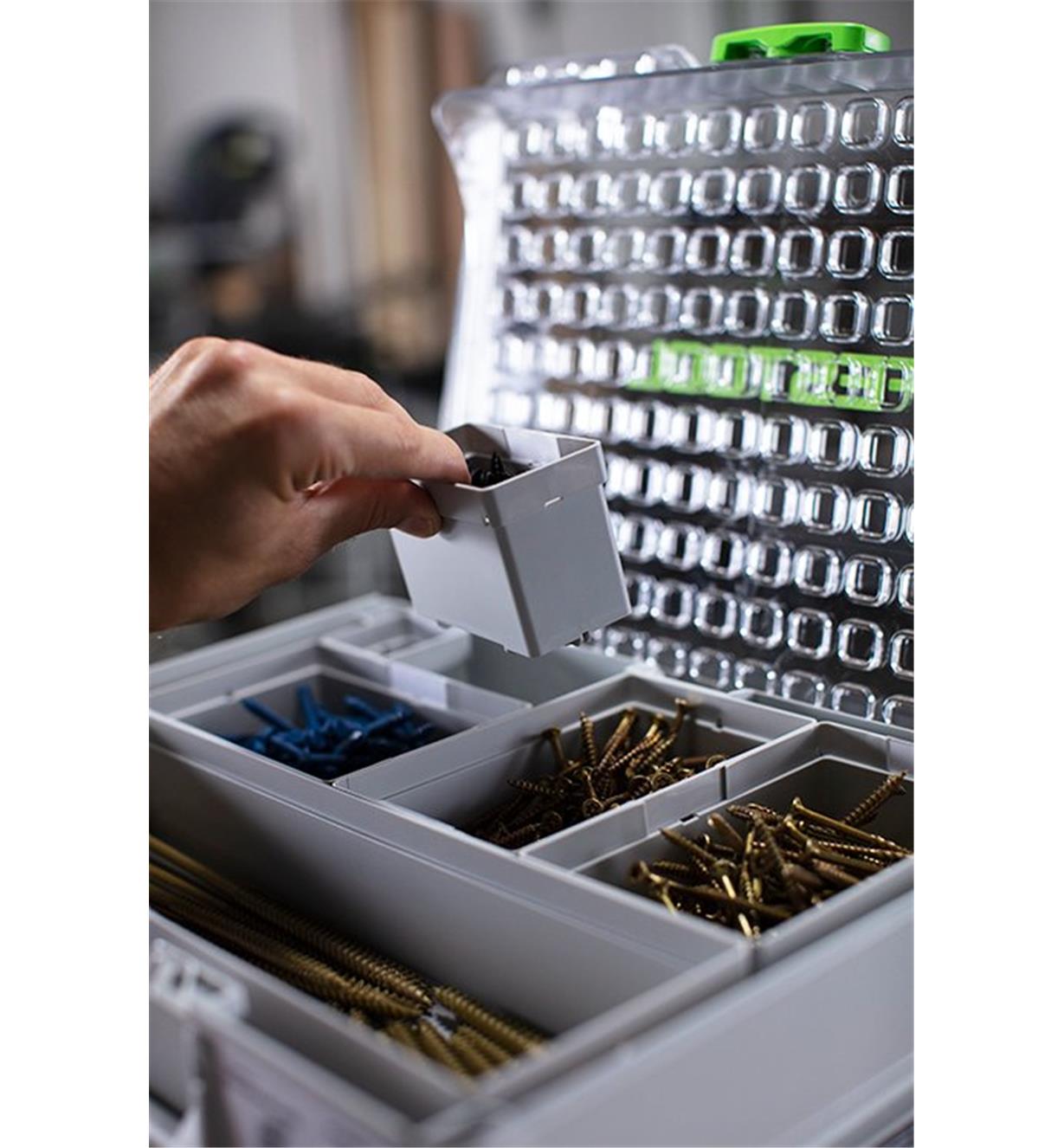 A bin is inserted into an open space in an organizer filled with bins containing hardware
