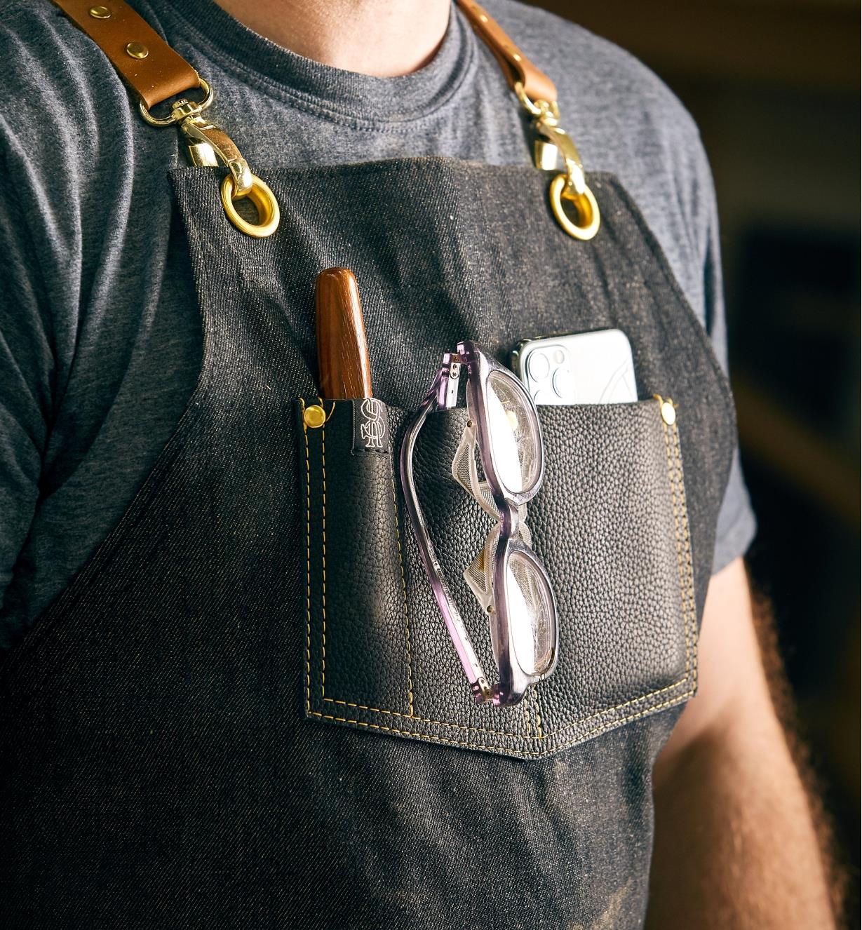 Chest pocket of the All-Purpose Apron holding a carving gouge, safety glasses and a cellphone