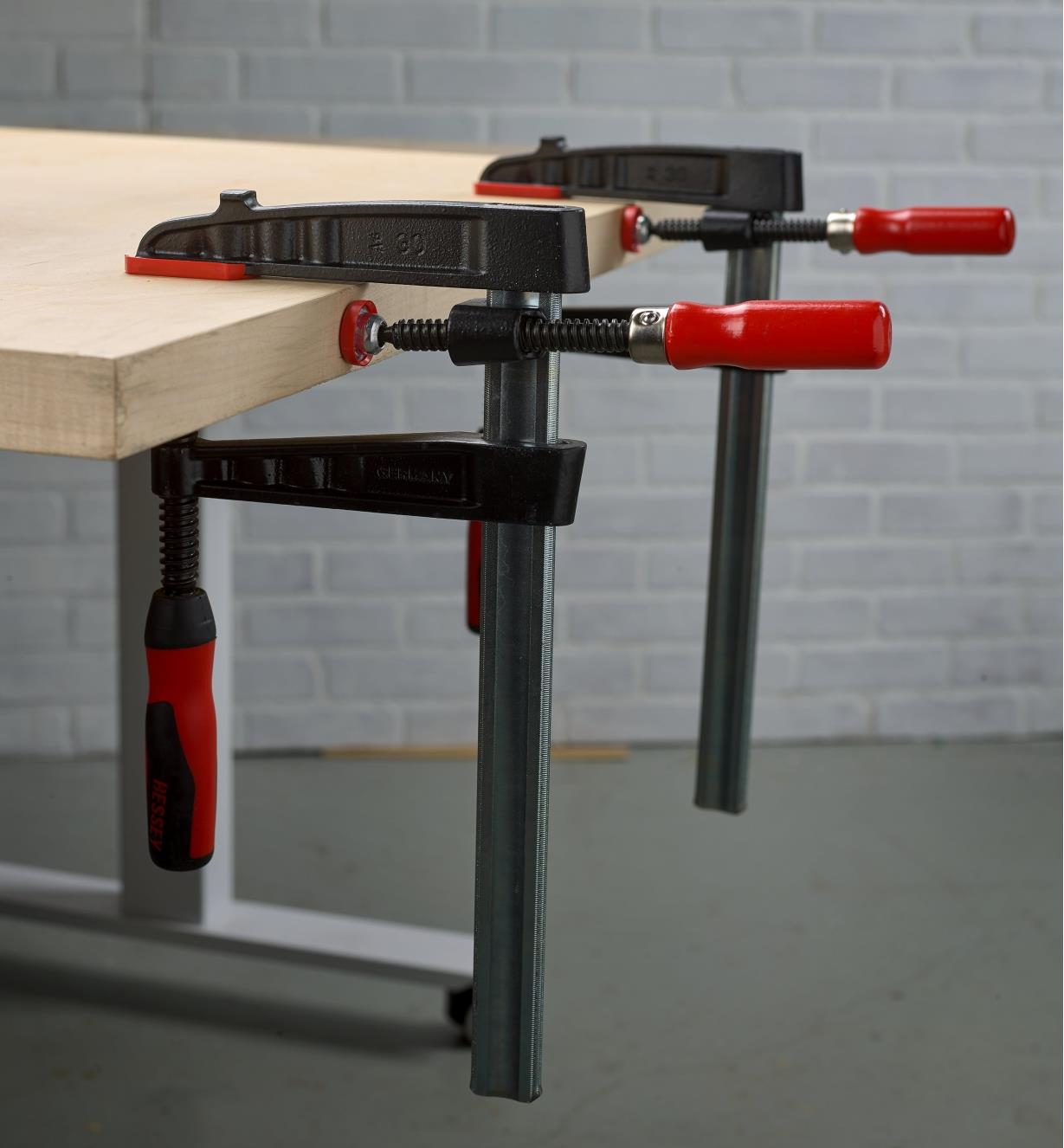 Two Bessey single-spindle edge clamps used with a Bessey fast-acting clamp used to clamp a strip of wood to the edge of a panel