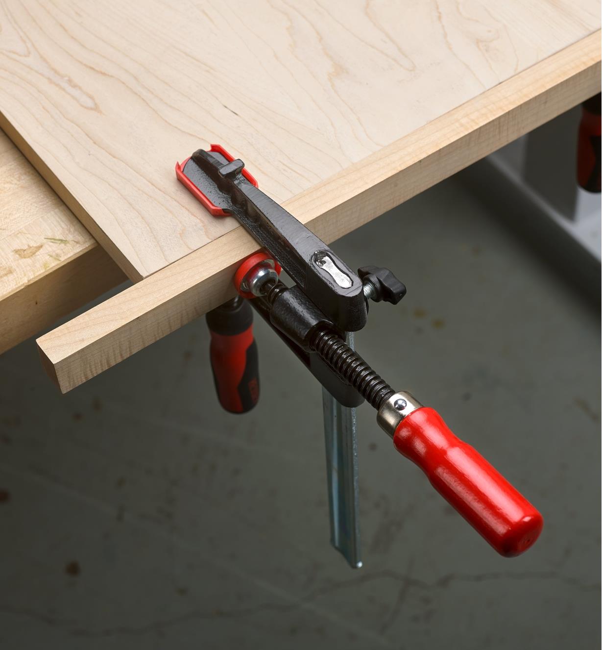 A Bessey single-spindle edge clamp connected to a Bessey fast-acting clamp, holding a strip of wood to the edge of a panel
