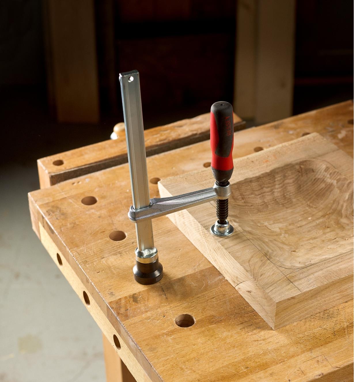 A Bessey hold-down clamp with a straight handle clamping a block of wood to a bench