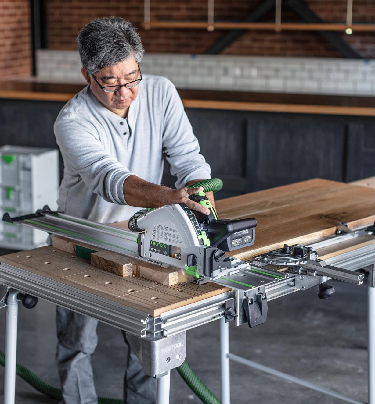 A worker using a TSC 55 KEBI-F track saw and a guide rail to cut wooden planks