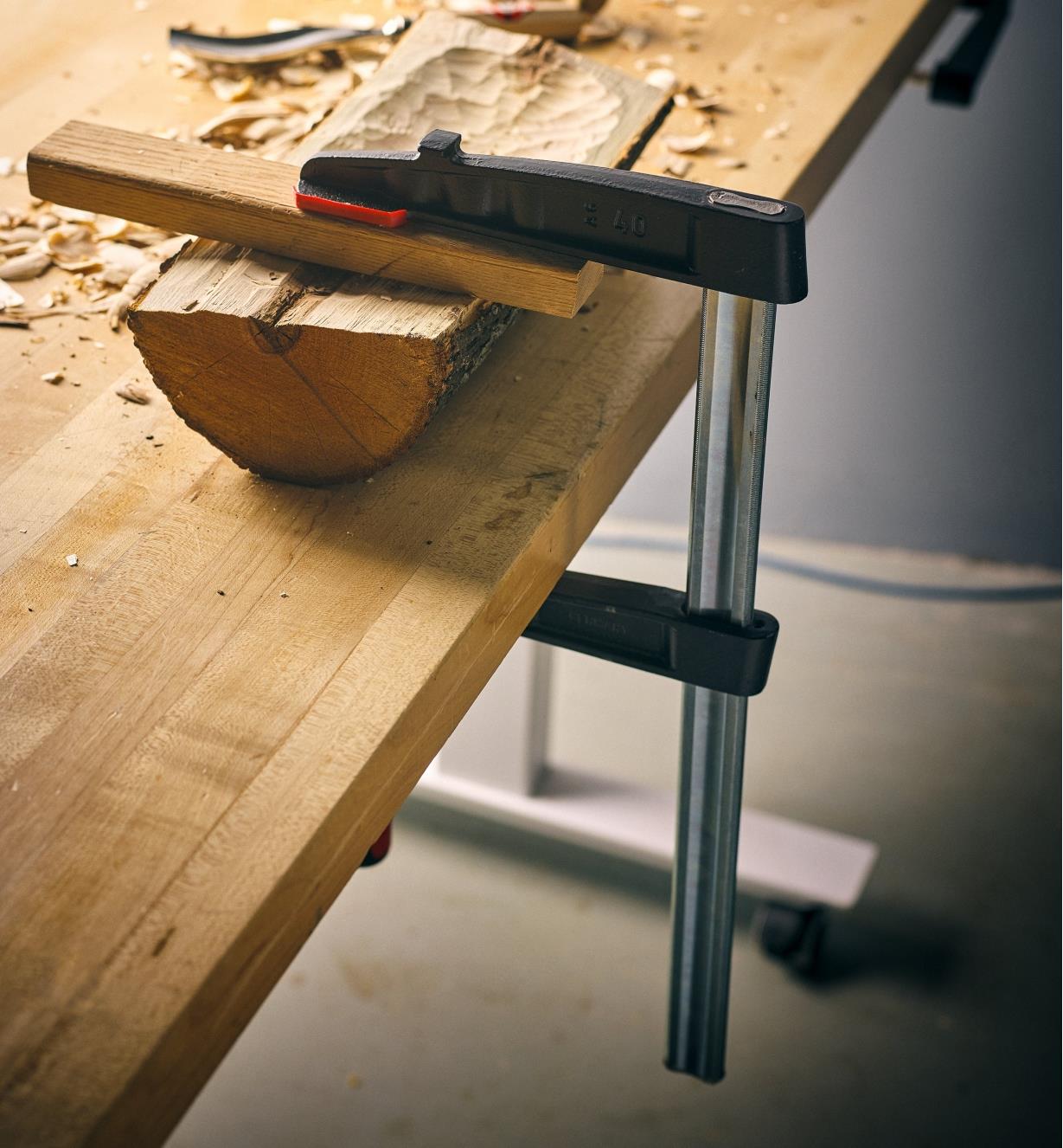 A Bessey 7" medium-duty FA clamp clamping a halved log to a workbench