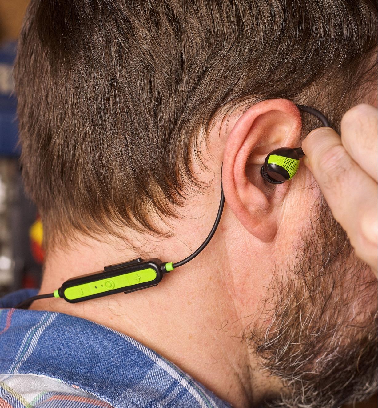 Personne plaçant un écouteur antibruit ISOTunes PRO Aware dans son oreille, avec le fil passant autour de l’oreille