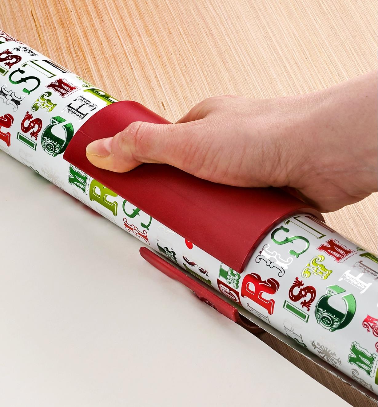 The sliding gift-wrap cutter being used to slice a piece of gift wrap neatly from the roll