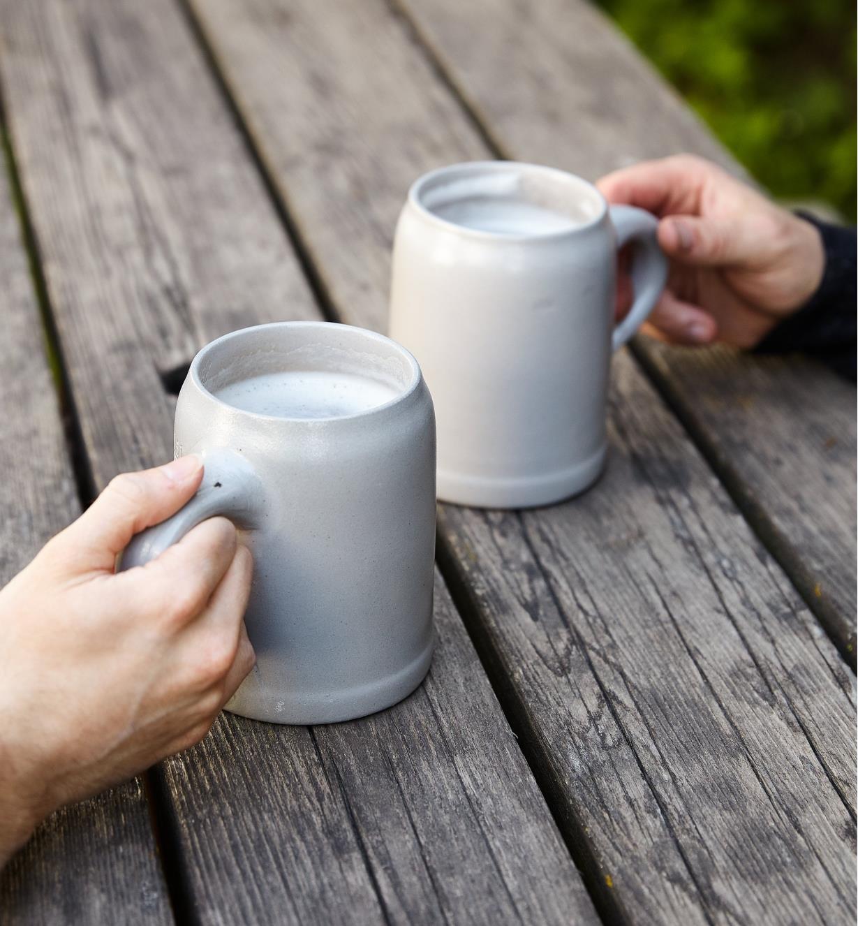 Two people hold Keferloher Beer Steins on an outdoor table